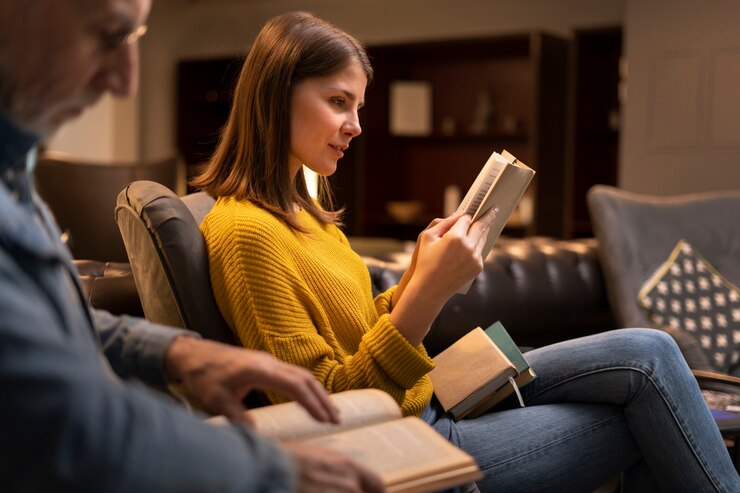 Woman in yellow sweater reading a book indoors, symbolizing introspection and personal spiritual growth at Valstella